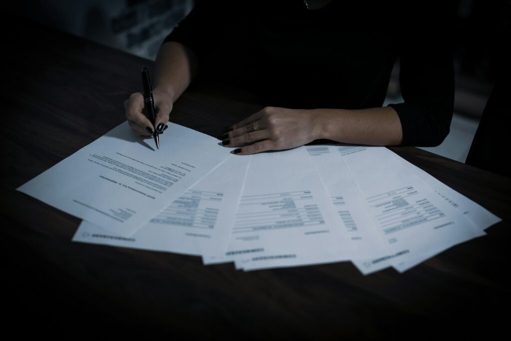 Une main féminine, avec un stylo, signe des documents isolés sur une table, mettant en avant une ambiance professionnelle et sérieuse.